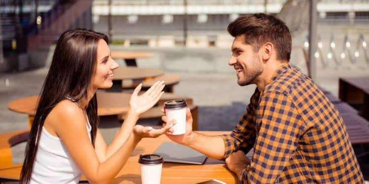Homem e mulher conversam em uma cafeteria ao ar livre, representando comunicação em espanhol.