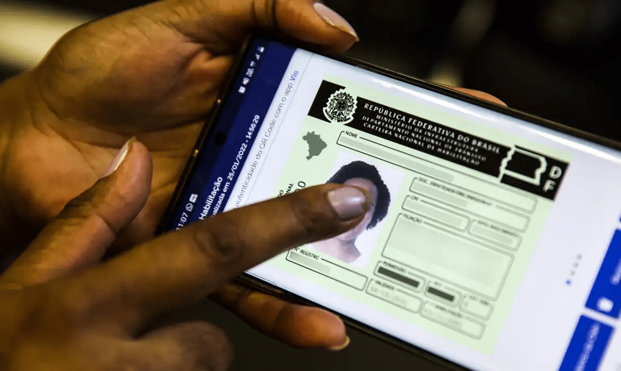 Pessoa acessando Carteira Nacional de Habilitação digital no smartphone com o dedo na foto.