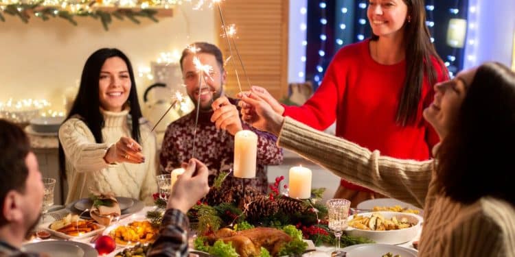 Grupo de amigos e familiares reunidos em volta de uma mesa de jantar decorada, segurando velas faíscas (sparklers) acesas durante uma ceia festiva.