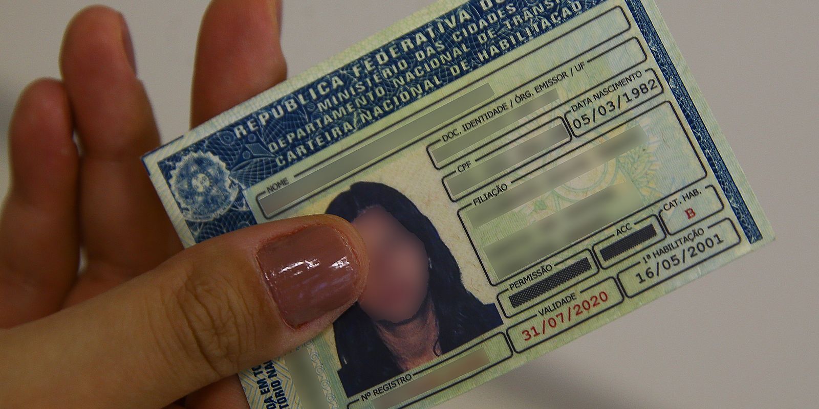 Cédula da Carteira Nacional de Habilitação (CNH) sendo segurada, representando o documento que se tornou mais acessível após as novas regras de 2025, com aulas gratuitas e redução de custos obrigatórios.