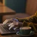 Mãos digitando em laptop sobre mesa de madeira com xícara de café ao lado à noite