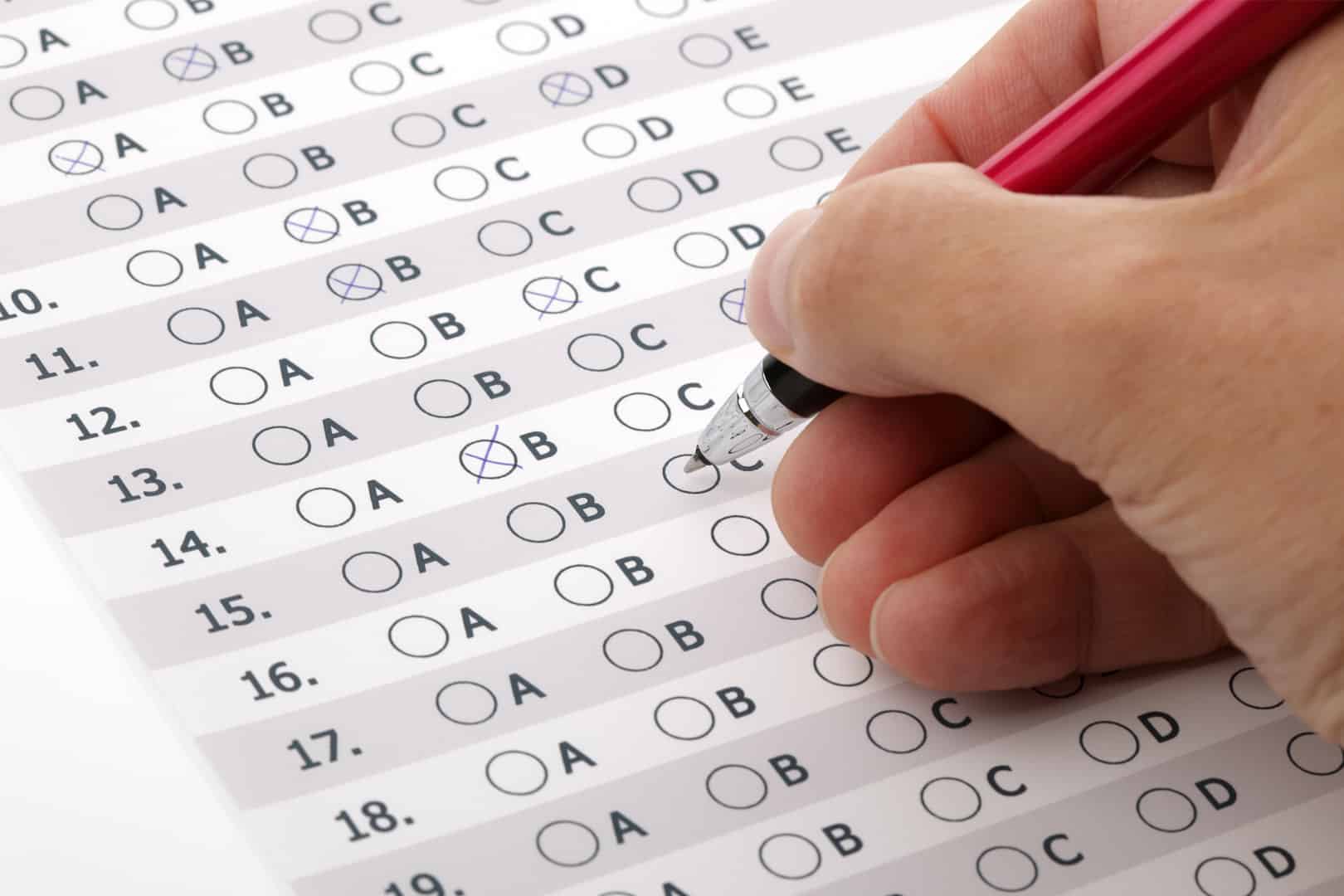 Mão preenchendo uma resposta de prova de múltipla escolha com caneta preta