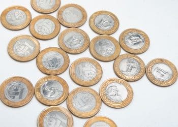 Diversas moedas de 1 Real espalhadas sobre uma superfície branca, mostrando diferentes faces e anos de fabricação.