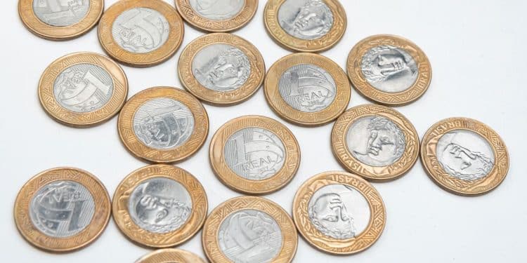 Diversas moedas de 1 Real espalhadas sobre uma superfície branca, mostrando diferentes faces e anos de fabricação.