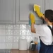 Mulher usando luvas amarelas limpando armário de cozinha cinza com pano branco