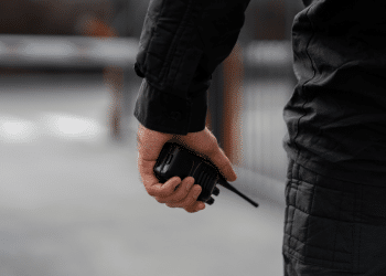 Mão segurando rádio comunicador preto durante serviço de segurança