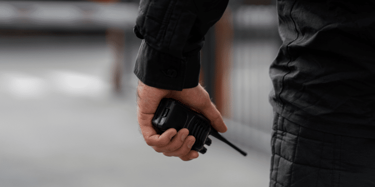 Mão segurando rádio comunicador preto durante serviço de segurança