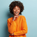 Mulher negra jovem com cabelo afro usando suéter laranja sorrindo com fundo azul claro