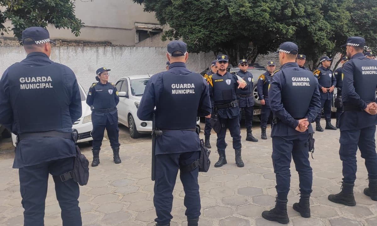 Grupo de guardas municipais em uniforme azul escuro reunidos em área externa para instrução