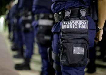 Guarda Municipal vestindo uniforme azul com bolsa tática preta na perna durante formação ou ronda.