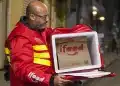 Homem usando jaqueta vermelha de entregador iFood segurando mochila térmica aberta com embalagem de papel iFood