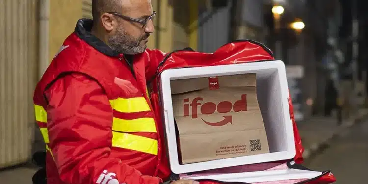 Homem usando jaqueta vermelha de entregador iFood segurando mochila térmica aberta com embalagem de papel iFood