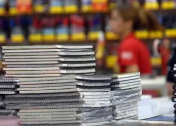 Pilha organizada de cadernos espiral com capas brancas e coloridas em papelaria com fundo desfocado