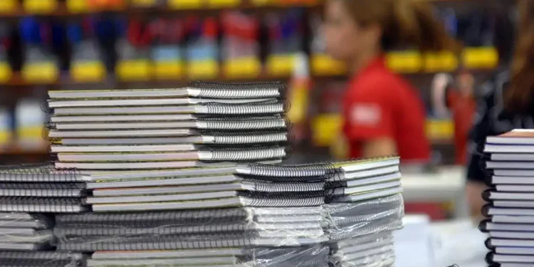 Pilha organizada de cadernos espiral com capas brancas e coloridas em papelaria com fundo desfocado