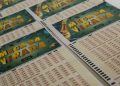 Close de vários bilhetes oficiais da Mega da Virada espalhados sobre uma mesa, exibindo o logotipo dourado do sorteio e as tabelas de números para marcação.