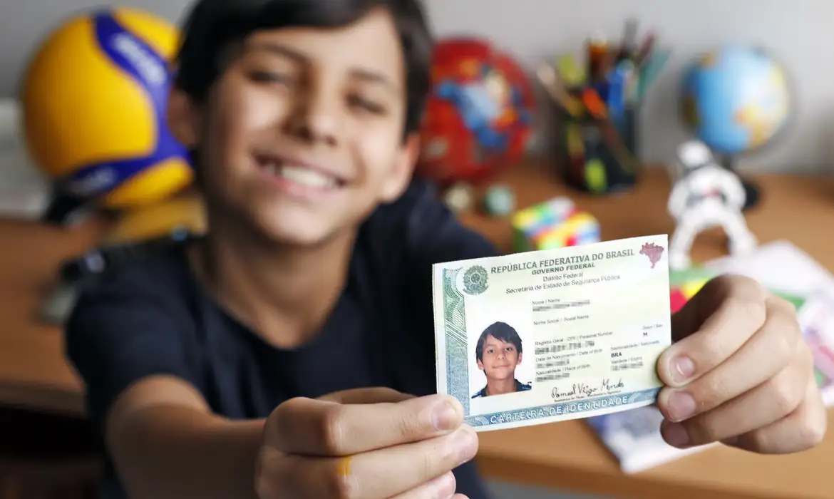 Criança segurando o documento de identidade (RG). A imagem representa a emissão da segunda via para menores de 16 anos, que precisam da presença do responsável legal.