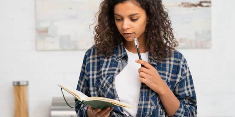 Pessoa pensativa segurando um caderno e uma caneta, refletindo sobre suas metas e objetivos.