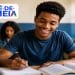 Estudante sorrindo enquanto escreve em um caderno em sala de aula, ao lado do logo do Pé-de-Meia, programa que paga R$ 200 pela participação no Enem a alunos da EJA