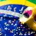 Máscara dourada decorada com detalhes em rosa e glitter sobre bandeira do Brasil decorada com confetes coloridos
