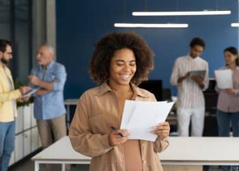 Mulher alegre segurando papéis com gráficos em escritório moderno com equipe ao fundo
