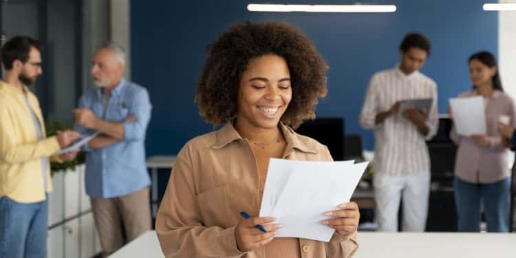 Mulher alegre segurando papéis com gráficos em escritório moderno com equipe ao fundo