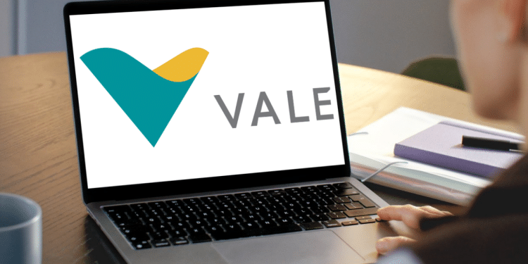 Pessoa olhando para o logo da Vale exibido em um notebook aberto sobre a mesa