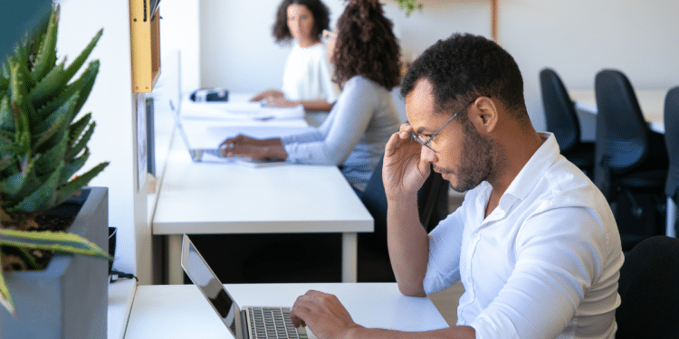 Jovens profissionais diversos trabalhando concentrados em laptops em escritório com decoração moderna e plantas