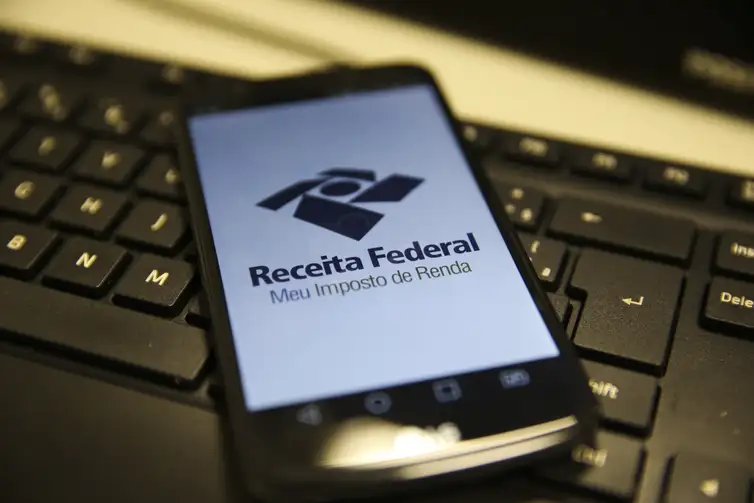 Aplicativo Receita Federal para Imposto de Renda Smartphone exibindo logo da Receita Federal do Brasil e texto Meu Imposto de Renda na tela, sobre teclado de computador