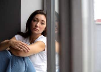 Jovem mulher triste ou introspectiva sentada em casa (Sinais de baixa autoestima por tentar agradar os outros)