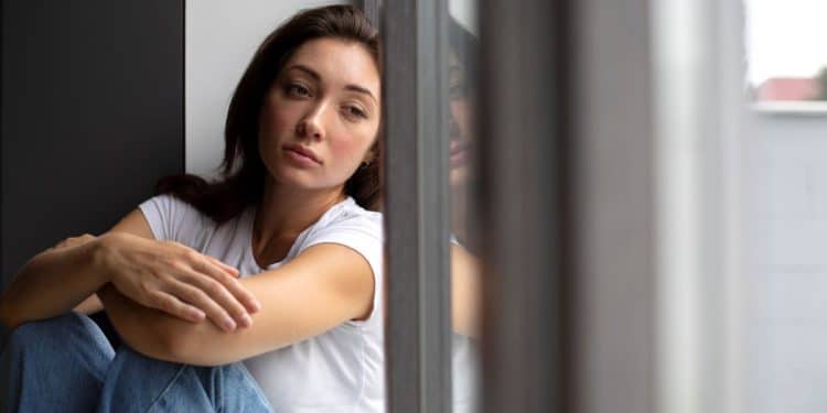 Jovem mulher triste ou introspectiva sentada em casa (Sinais de baixa autoestima por tentar agradar os outros)