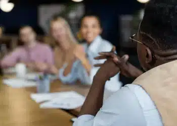 Grupo de pessoas em uma reunião de escritório, com um participante falando enquanto os outros escutam.