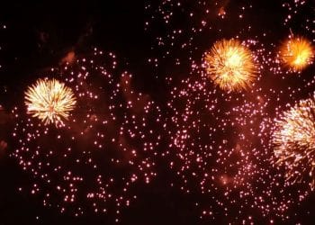 Fogos de artifício dourados brilhando e explodindo contra um céu escuro durante uma celebração noturna.