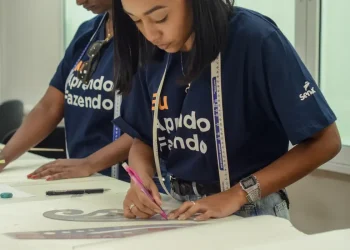 Jovem mulher trabalhando com régua e lápis em mesa, vestindo camiseta azul do Senai