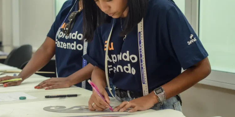 Jovem mulher trabalhando com régua e lápis em mesa, vestindo camiseta azul do Senai