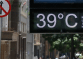 Placa digital mostrando temperatura de 39 °C em uma rua movimentada durante dia quente