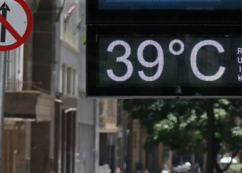 Placa digital mostrando temperatura de 39 °C em uma rua movimentada durante dia quente