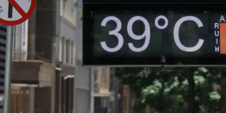 Placa digital mostrando temperatura de 39 °C em uma rua movimentada durante dia quente