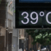 Placa digital mostrando temperatura de 39 °C em uma rua movimentada durante dia quente