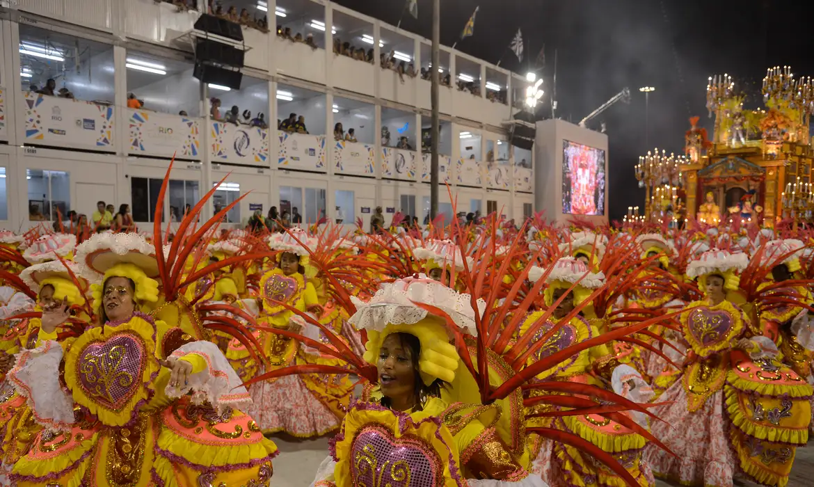 Carnaval 2026 calendário. Ala de escola de samba desfila com fantasias amarelas e vermelhas durante apresentação do Carnaval 2026.