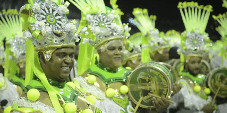 Passistas em desfile de carnaval com fantasias verde e prata, representando as festividades de 2026