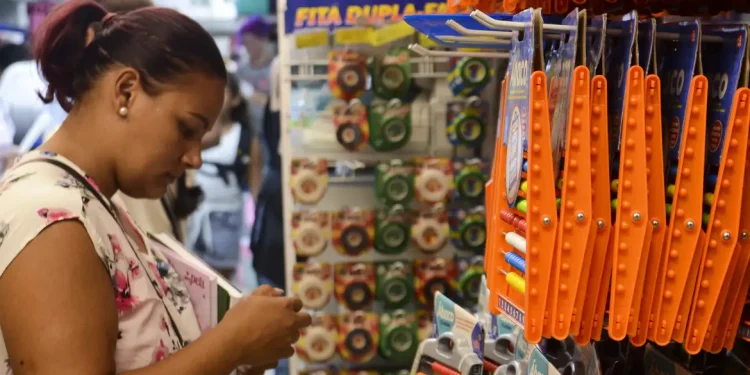 Mulher analisando produtos escolares em prateleira com fitas coloridas e réguas laranja à venda
