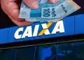 Mão segurando notas de R$100 em frente à fachada da agência da CAIXA, representando o saque do FGTS.