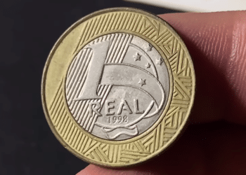 Reverso de uma moeda de 1 Real do ano 1998, mostrando o valor facial sobre o núcleo prateado e o anel dourado com grafismos indígenas.