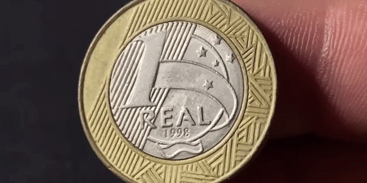 Reverso de uma moeda de 1 Real do ano 1998, mostrando o valor facial sobre o núcleo prateado e o anel dourado com grafismos indígenas.
