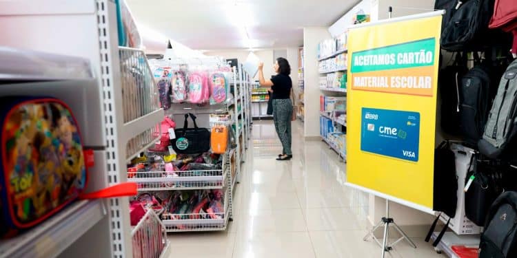 Loja de papelaria com banner indicando aceitação do Cartão Material Escolar do GDF com bandeira Visa.