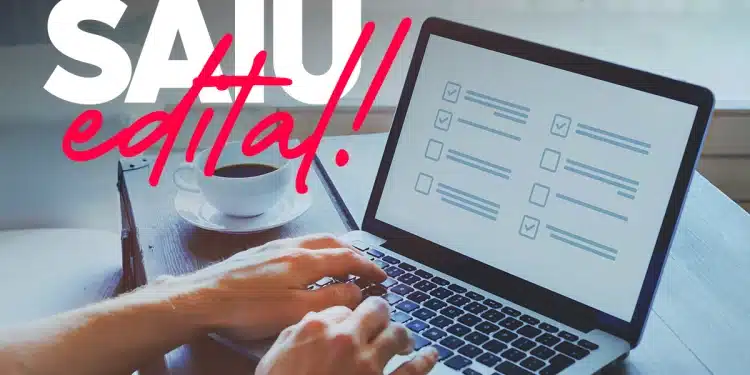 Mãos digitando em notebook com tela de checklist, café ao lado e texto “SAIU edital!” em destaque.