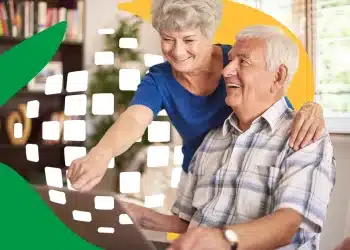 Casal de idosos usando notebook em casa, sorrindo, inclusão digital para idosos