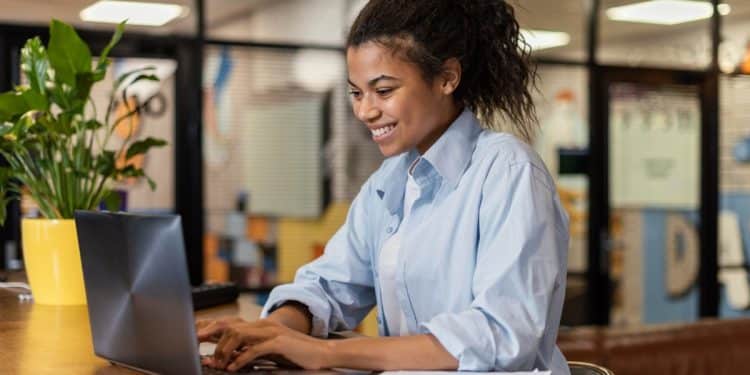 Jovem sorridente digitando em notebook durante curso de qualificação profissional gratuito