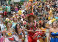 Grupo de foliões fantasiados com flores e adereços coloridos sorrindo durante bloco de Carnaval de rua