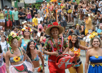 Grupo de foliões fantasiados com flores e adereços coloridos sorrindo durante bloco de Carnaval de rua